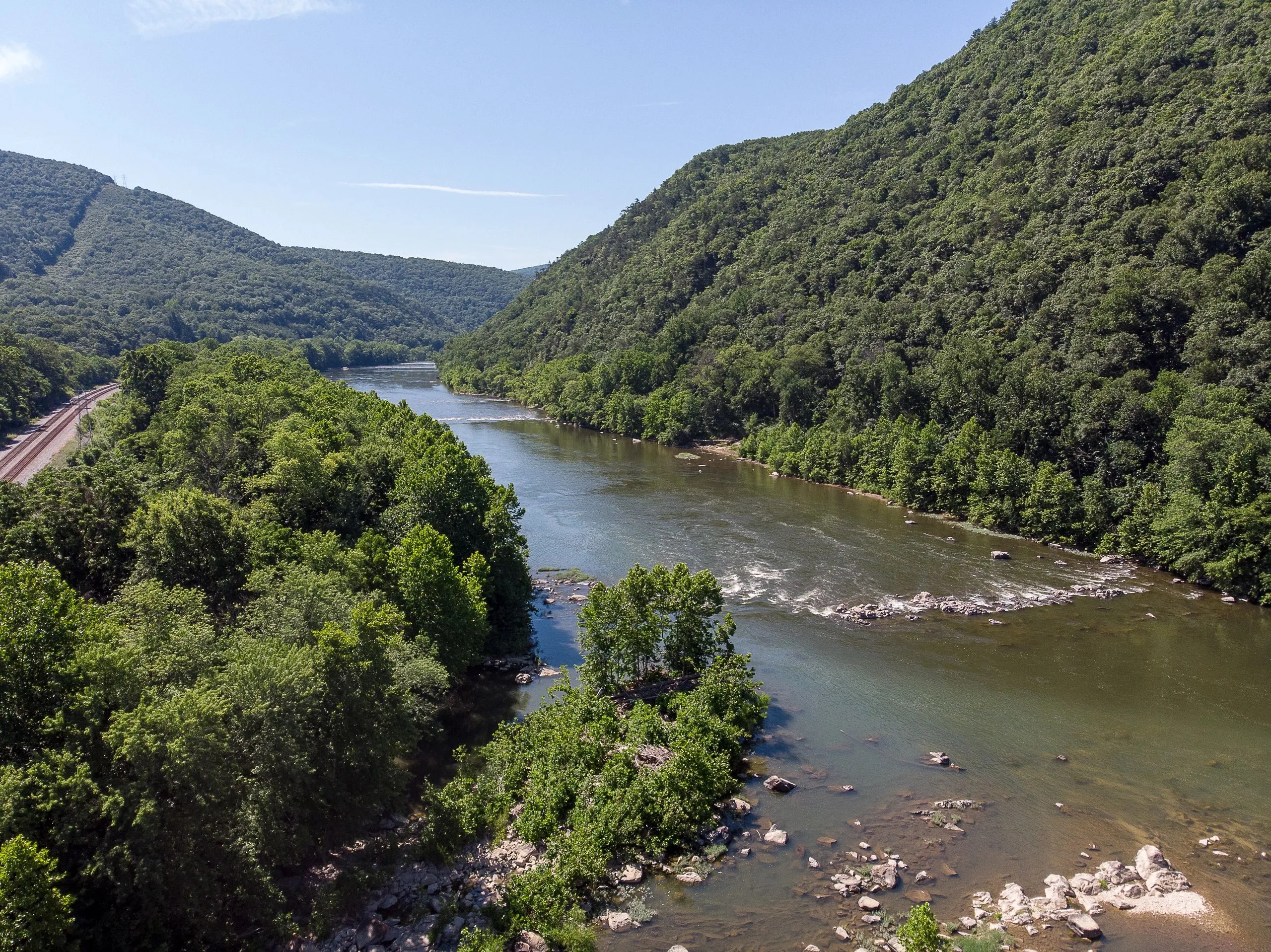 A river with rocky banks running between forested hillsides in summer.